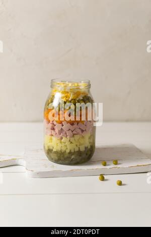 Zutaten für Olivier Salat russisch in einem Glas mit einem Löffel auf weißem Hintergrund. Russische Küche. Speicherplatz kopieren. Vertikale Ausrichtung. Stockfoto