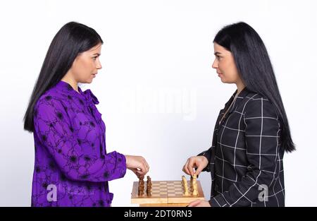 Ernsthafte weibliche Zwillinge spielen Schach und schauen Auge in Auge auf einem weißen Hintergrund. Schachspiel-Konzept Stockfoto