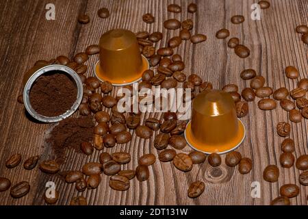 Öffnen Sie die Espresso-Kaffeekapsel mit gemahlener Kaffeepulver im Inneren. Kaffeepads und geröstete Kaffeebohnen auf Holzhintergrund. Hochwertige Fotos Stockfoto