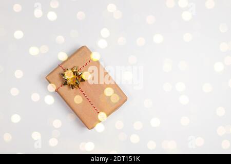 Weihnachten und Neujahr Urlaub Hintergrund. Überraschungs-Geschenkschachtel in Bastelpapier mit Goldschleife und Dekoration festliche goldene Glitzer auf weißem Tisch eingewickelt. Flach liegend, Draufsicht. Stockfoto