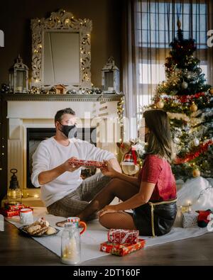 Weihnachtspaar trägt Maske während der Weihnachtsnacht, Nahaufnahme Porträt von glücklichen Mixed-Rennen Paar mit weihnachtsgeschenken und das Tragen von medizinischen Masken in Quarantäne. Paar mit Gesichtsmaske während covid Ausbruch Pandemie Stockfoto