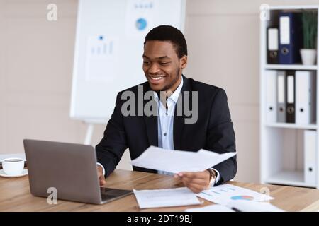Glücklicher schwarzer Geschäftsmann, der Berichte im modernen Büro überprüft Stockfoto