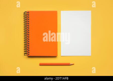 Orangefarbener Spiralnotizblock mit einem Blatt weißem Papier und Orangefarbener Bleistift auf gelbem Hintergrund Stockfoto