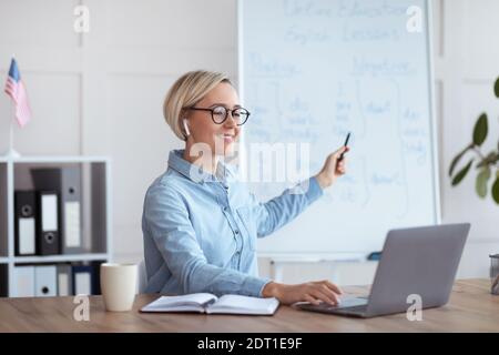 Junge Lehrerin, die Online-Englischunterricht auf Laptop, zeigt auf Tafel, erklärt Grammatik Regeln Stockfoto