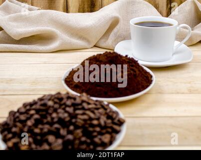 Drei Stufen der Zubereitung von gemahlenem Kaffee, Getreide, Getränk. Kaffeezutaten. Geröstete Kaffeesorten auf dem Hintergrund von Tassen mit Kaffee Stockfoto