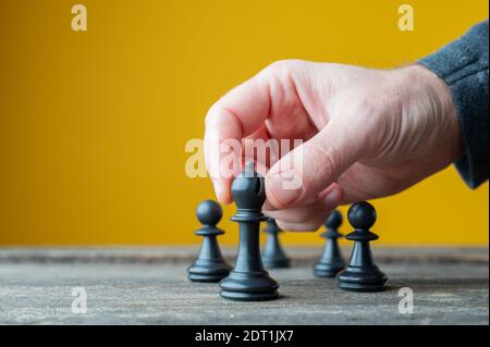 Männliche Hand positioniert schwarze Schachfigur vor den anderen in einem konzeptuellen Bild von Führung und Macht. Stockfoto