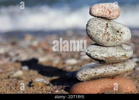 Balancierende Steine: Ein farbenfroher Steinhaufen, der übereinander balanciert ist, mit einem Kiesstrand und einer Welle, die im Hintergrund am Ufer bricht Stockfoto