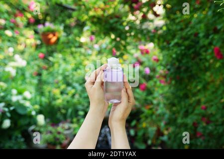 Die Hände der Frau halten Gesichtswasser Flasche auf einem blühenden natürlichen Hintergrund. Stockfoto