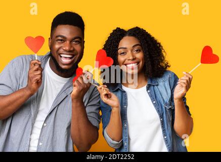 Wir feiern den Valentinstag. Liebevolles schwarzes Paar mit roten Papierherzen auf Stäbchen Stockfoto