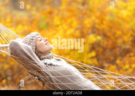 Profil einer glücklichen Frau, die auf einer Seilhängematte liegt In der Herbstsaison im Wald Stockfoto