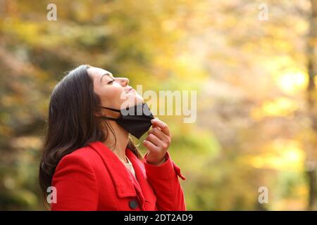 Profil einer Frau, die Schutzmaske auszieht, um zu atmen Frische Luft in einem Park in covid Zeiten Stockfoto