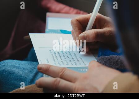 Hand der Person, die Postkarte mit Stift füllt. Nahaufnahme. Stockfoto
