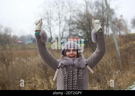 Eine Frau im Winter Kleidung Spaziergänge im Park. Triumphierend hob sie die Hände und schreit freudig. Stockfoto