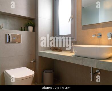 Modernes Interieur mit kleinem Badezimmer, gefliestem grauem Stein mit Fenster, Waschbecken, Spiegel-Rücklicht, an der Wand hängende Toilette Stockfoto