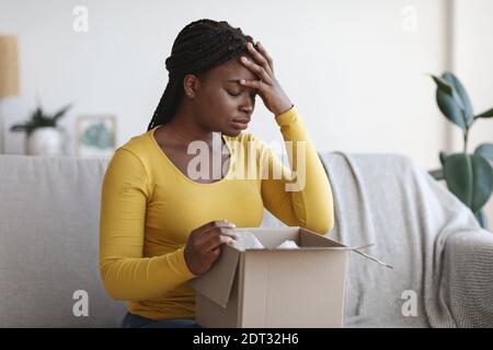 Falsches Paket. Verärgert afroamerikanische Frau sitzt mit ausgepackten Box zu Hause Stockfoto