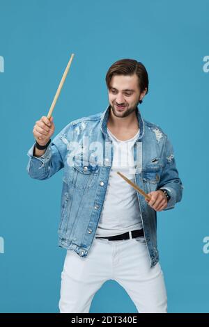 Glücklich schöner männlicher Schlagzeuger improvisiert isoliert auf blauem Studiohintergrund Stockfoto