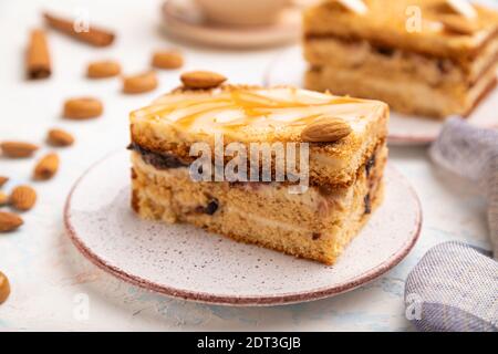 Honigkuchen mit Milchcreme, Karamell, Mandeln und einer Tasse Kaffee auf weißem Betonboden und Leinentextilien. Seitenansicht, selektiver Fokus, nah U Stockfoto
