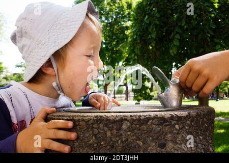 Kleiner Junge, der aus einem Brunnen im Park trinkt Stockfoto