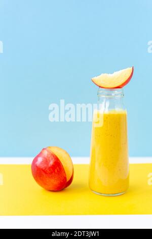 Gelber Smoothie in einem Glas, eine Scheibe Nektarine auf gelbem, himmelblauem Hintergrund. Gesunde Ernährung, Entgiftung, vegan. Stockfoto