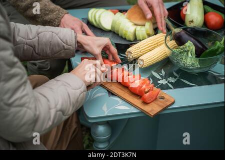 Freudige Anstrengungen, um für einen Familienurlaub im Hof vorzubereiten. Hände eines Mannes und einer Frau, die Gemüse für das Grillen für ein Picknick vorbereiten. Ohne Gesicht Stockfoto