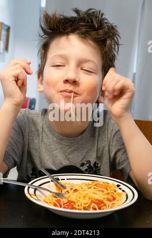 Fröhlicher Junge essen Nudeln o Tisch Stockfoto