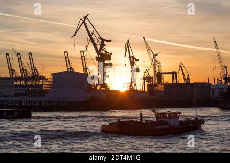 Die untergehende Sonne scheint hinter KrŠnen auf der Werft von Blohm + Voss, aufgenommen von der LandungsbrŸcken im Hamburger Hafen. Stockfoto