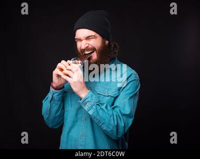 Keine Diät. Bärtiger Hipster-Mann in blauem Hemd, der dunkle Schokolade über sich isst. Stockfoto