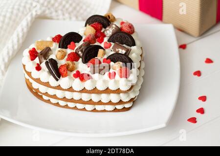 Herzförmiger Kuchen mit Ricotta und Schlagsahne, verziert mit Schokolade, Waffeln, Keksen und Erdbeeren Stockfoto