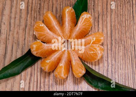 Süße Mandarinenscheiben und Blätter liegen auf einem Holztisch Stockfoto