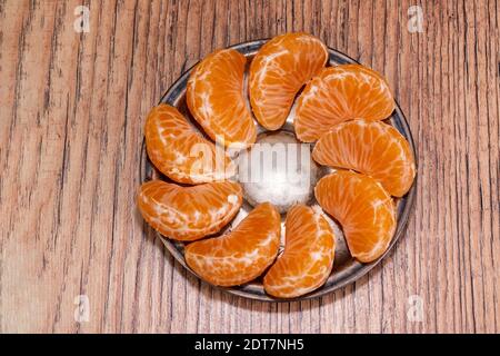 Auf einem Holztisch liegen Tangerinesteiben, die auf einer bronzenen Untertasse ordentlich angeordnet sind Stockfoto