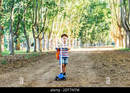 Lächelndes Kind auf Kick Scooter in der Landschaft. Outdoor-Aktivitäten für Kinder auf sicheren ländlichen Straße. Kinder lernen Rollbrett Skaten. Kleiner Junge Witz Stockfoto