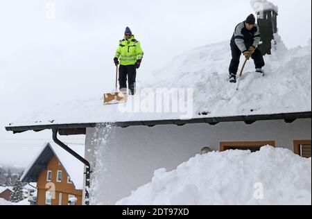 Zwei Männer schaufeln hohen schweren Schnee von einem Hausdach Stockfoto