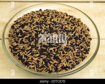 Würzen Kümmel und Nigella in einer Glasplatte auf einem Holzhintergrund Stockfoto