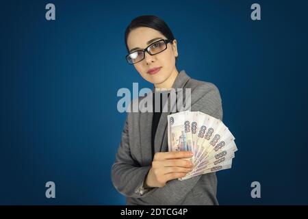 Schöne junge Frau in Brille hält eine Menge russischer Rubel in den Händen. Stockfoto
