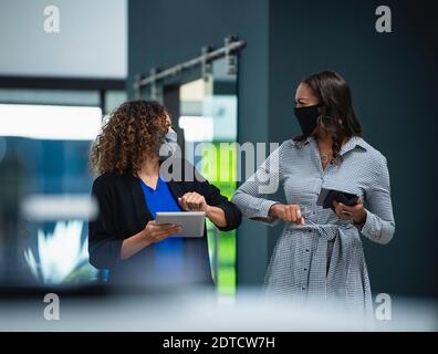 Geschäftsfrauen in Gesichtsmasken Gruß mit Ellbogen im Büro Stockfoto