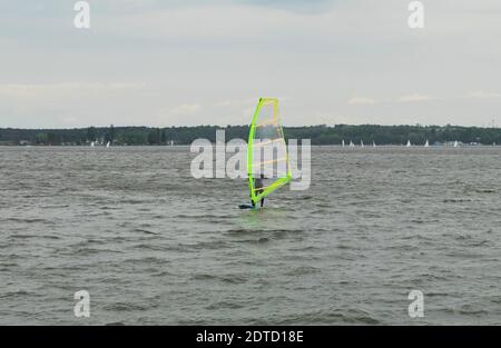 Der Athlet fährt auf einem Brett mit einem Segel auf dem Wasser. Kitesurfer reitet auf dem Wasser in einem kleinen Teich. Stockfoto