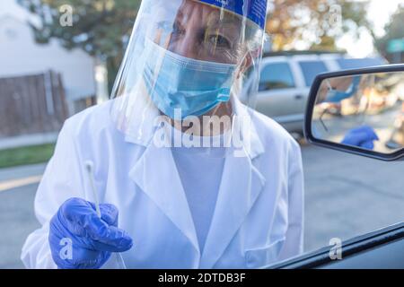 Medizinisches Personal in Schutzkleidung nähert sich dem Auto mit Coronavirus Abstrichtest Stockfoto