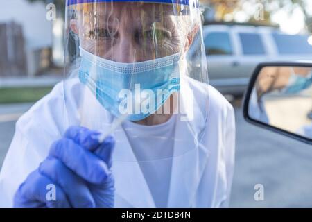 Medizinisches Personal in Schutzkleidung nähert sich dem Auto mit Coronavirus Abstrichtest Stockfoto