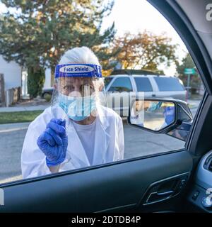 Medizinisches Personal in Schutzkleidung nähert sich dem Auto mit Coronavirus Abstrichtest Stockfoto