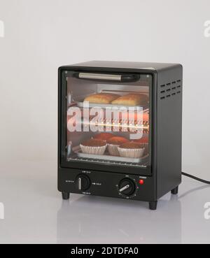 Elektrischer kleiner Küchenofen mit Brot und Tassenkuchen isoliert Auf weißem Hintergrund Stockfoto