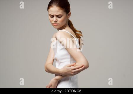 Rothaarige Frau in einem weißen T-Shirt auf beigem Hintergrund Gestikulieren mit ihren Händen Schmerzen im Ellbogen Stockfoto