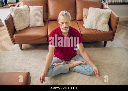 Grauhaariger Mann, der in einer Lotuspose auf dem Boden sitzt Stockfoto