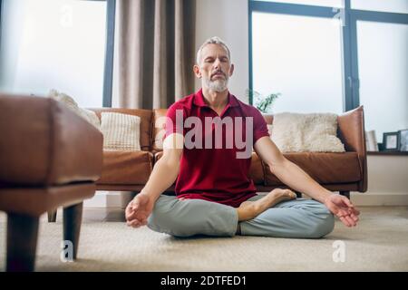 Grauhaariger Mann, der in einer Lotuspose auf dem Boden sitzt Stockfoto