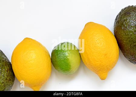 Tisch mit Zitronen, Limette und Avocado in diagonaler Reihe auf weißem Hintergrund. Stockfoto