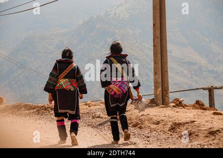 Frauen aus dem Stamm der Hmong tragen ihre traditionelle Kleidung, während sie zum Dorf Lao Cai in Sa pa, Vietnam, zurückwandern Stockfoto