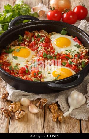 Georgische Frühstück Spiegelei mit Tomaten, Zwiebeln und Walnüssen Nahaufnahme in einer Pfanne auf dem Tisch. Vertikal Stockfoto