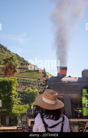 Schöne Landschaft mit einem Dampfzug auf dem Weg nach Pinhao in Portugal. Frau auf dem Rücken wartet auf den Zug Stockfoto