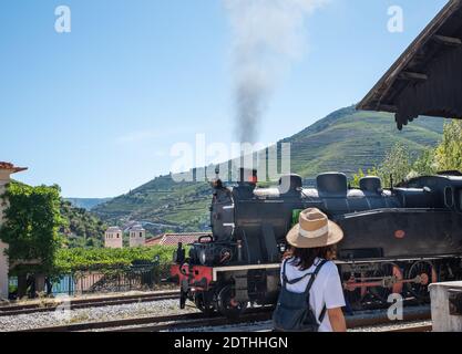 Schöne Landschaft mit einem Dampfzug auf dem Weg nach Pinhao in Portugal. Frau auf dem Rücken wartet auf den Zug Stockfoto