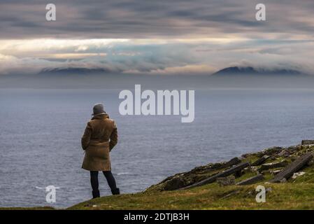 Frau, die vom Slieve League Berg an der Atlantikküste der Grafschaft Donegal, Irland, den Blick auf das Meer mit Bergen und die wunderschöne Wolkenlandschaft genießt Stockfoto