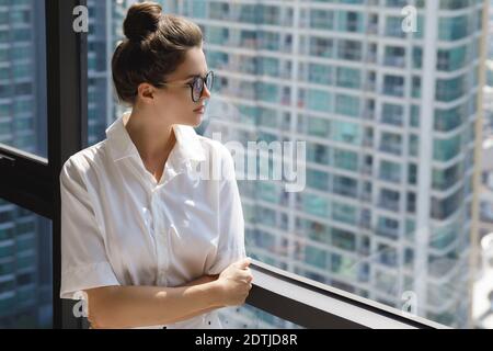 Junge Geschäftsfrau, die neben dem großen Fenster steht. Büro im modernen Gebäude der Großstadt Stockfoto